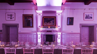 A formal banquet table set-up in a grand main hall with pink uplighters.