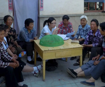 Group of people sat outside around a table. Some of them are holding pieces of paper and conversing.