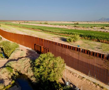 A border fence stretching into the distance over green land. 
