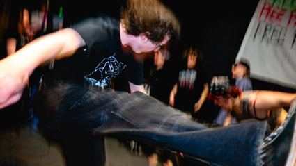 Person mid-air kick at a crowded indoor music venue, blurred motion.