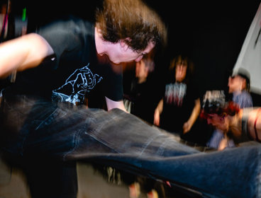 Person mid-air kick at a crowded indoor music venue, blurred motion.
