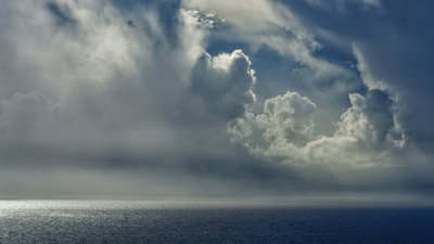Moody grey clouds forming over the sea, light bouncing off the edges of the clouds.