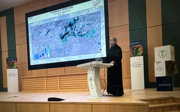 A woman on a podium giving a speech at a conference with behidn her a board that shows a map and the title Household Reservoirs South West Afghanistan from 2016 until 2019.