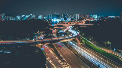 Timelapse photo of a highway with cars in the evening against a background of blue lit highrise buildings.