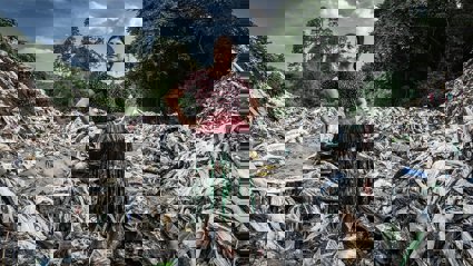 A person in traditional dress standing in a pile of plastic with hands on their hips.