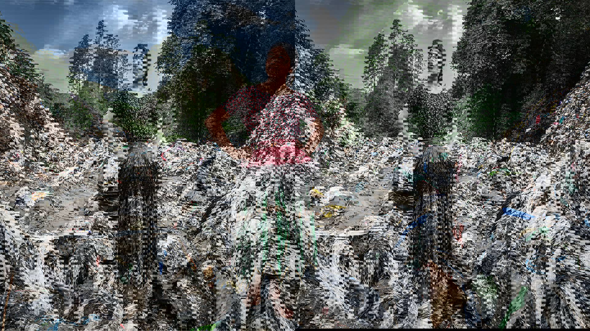 A person in traditional dress standing in a pile of plastic with hands on their hips.