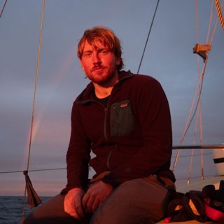 Will Jones, sat on a boat wearing a black, zip up jumper.