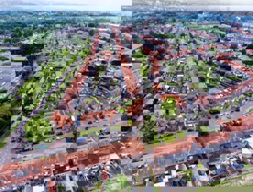 An aerial view of a suburban area of a town with orange roofs, green gardens and linear roads