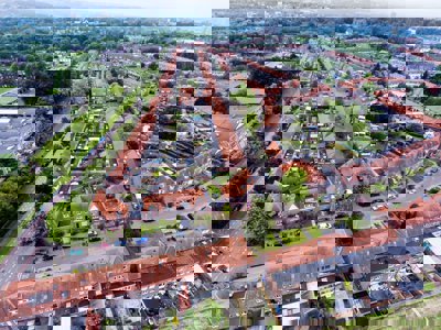 An aerial view of a suburban area of a town with orange roofs, green gardens and linear roads