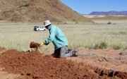 Man shovelling in red dirt which is part of a fairy circle in Namibia.