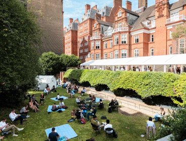 People sitting on the grass and standing inside a gazebo on a terrace outside the Society's building.