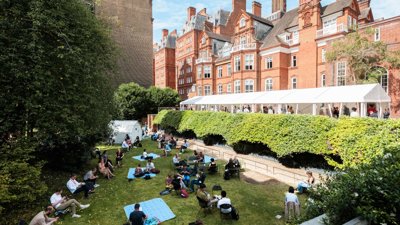 People sitting on the grass and standing inside a gazebo on a terrace outside the Society's building.