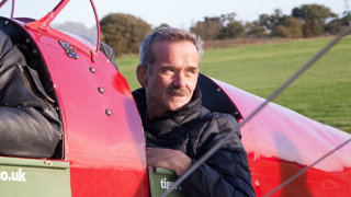 Man sitting in a fighter jet that is parked in a grass field.