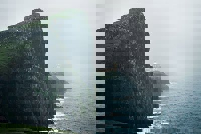 Cliff on the coastline with a lighthouse in the distance