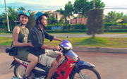 Two people on motorbike in Vietnam wearing helmets, and one with camera.