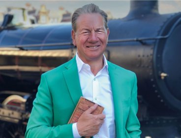 Person wearing green suit jacket stood in front of black train.