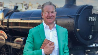 Person wearing green suit jacket stood in front of black train.