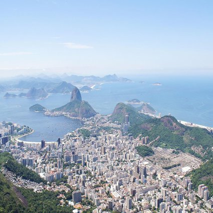A view over Rio de Janeiro showing a sprawling city located in the valley between green wooded hills, finishing at the ocean