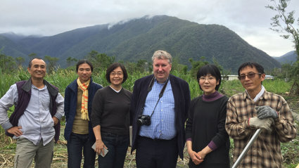 Group of people posing in a green rural field with misty mountains in the background. Michael Woods stand fourth from the left.
