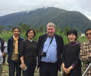 Group of people posing in a green rural field with misty mountains in the background. Michael Woods stand fourth from the left.