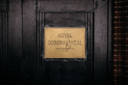 Dark wooden door with a gold-coloured metal sign that says Royal geographical Society. 
