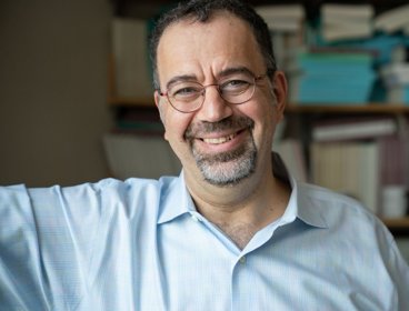 Headshot of Daron Acemoglu against bookshelf backdrop.