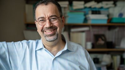 Headshot of Daron Acemoglu against bookshelf backdrop.