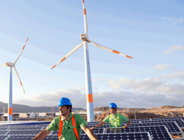 Two people amongst rows of solar panels and three wind turbines.
