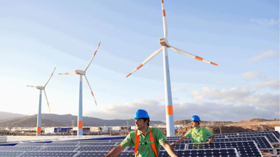 Two people amongst rows of solar panels and three wind turbines.