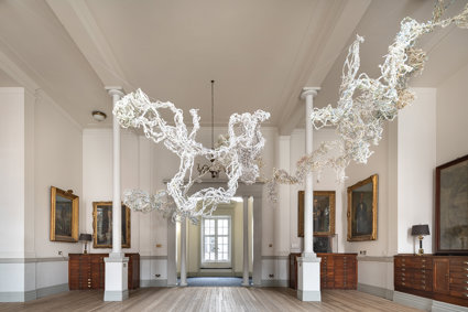 Art sculpture made of braided shredded paper, hanging in an ornate room with wooden floors and oil painting portraits