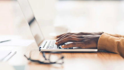 Closeup of a laptop and a person typing on the keyboard.