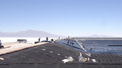 Construction workers laying out sheets of tarpaulin across an large artificial hole in an open, arid landscape.