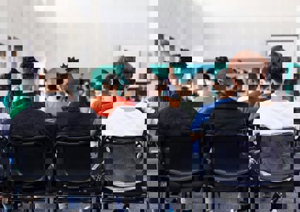 Students sitting in a classroom watching a teacher, viewed from behind