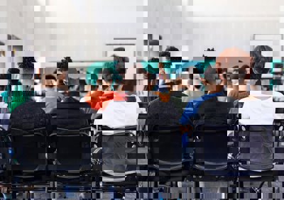 Students sitting in a classroom watching a teacher, viewed from behind