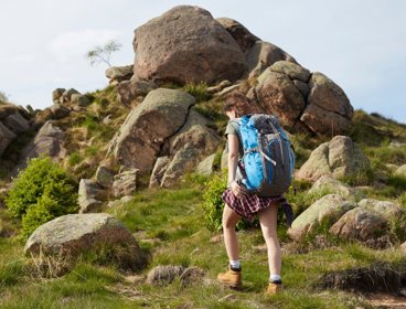 Person wearing rucksack walking a hill covered in large rocks in the countryside.