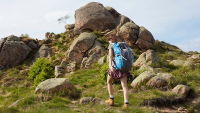 Person wearing rucksack walking a hill covered in large rocks in the countryside.