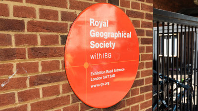 Large, round Royal Geographical Society with IBG entrance sign on a brick-wall.