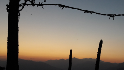 Wire fence in foreground. Mountains at sunset in background