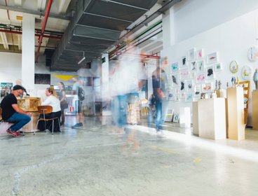 People moving around an exhibition with artwork hung on the walls and sculptures on stands.