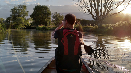 Person canoeing on river during sunset.