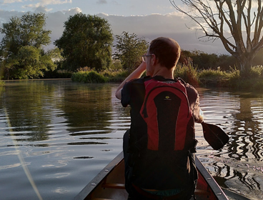 Person canoeing on river during sunset.