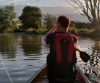 Person canoeing on river during sunset.