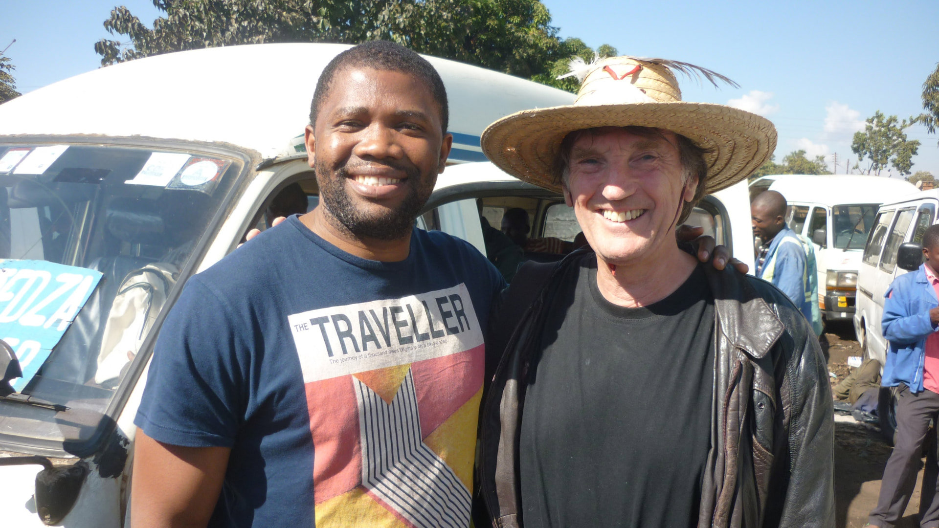 Two people smiling while posing for a photo, with vans in the background.