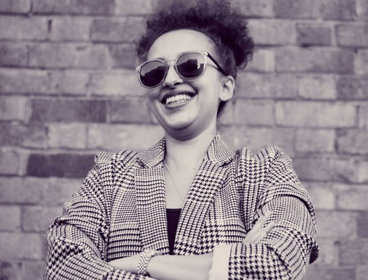 Person (Aurella Yussuf) standing against a brick wall smiling.