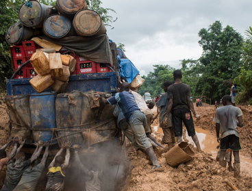 People pushing a large truck out of a muddy ditch. 