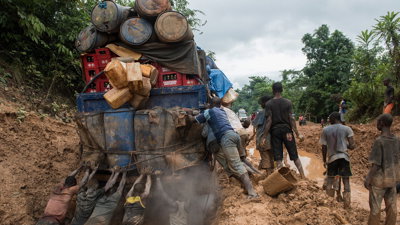People pushing a large truck out of a muddy ditch. 