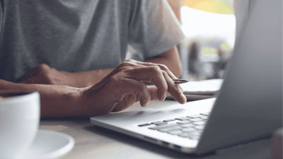 A hand holding a pen working over laptop cursor.