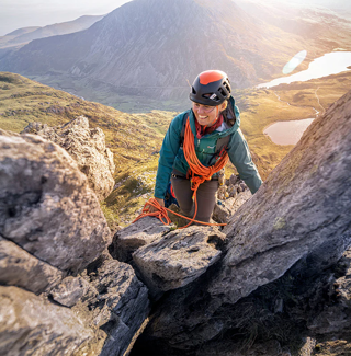Rebecca Coles in climbing gear climbing over a pile of boulders.