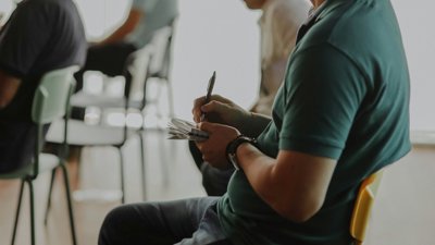 Person sat on chair writing in notebook.