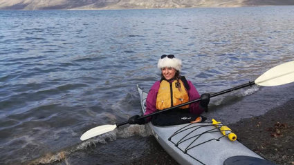 A person in a canoe on the edge of an expanse of water.